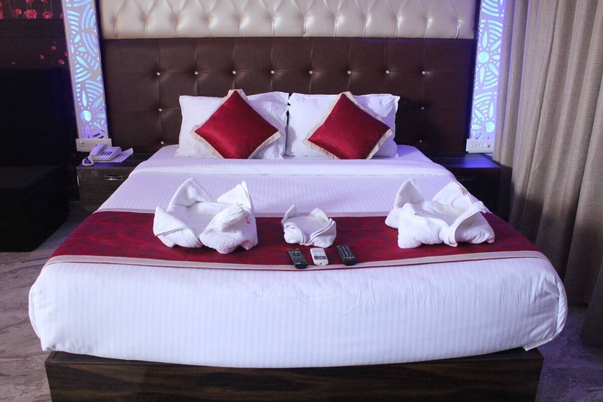 Een hotelkamer met een groot bed, twee rode kussens, een rode deken en meerdere handdoeken op het bed.