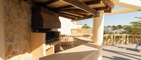 Un patio al aire libre con muro de piedra, pérgola de madera y chimenea de piedra.