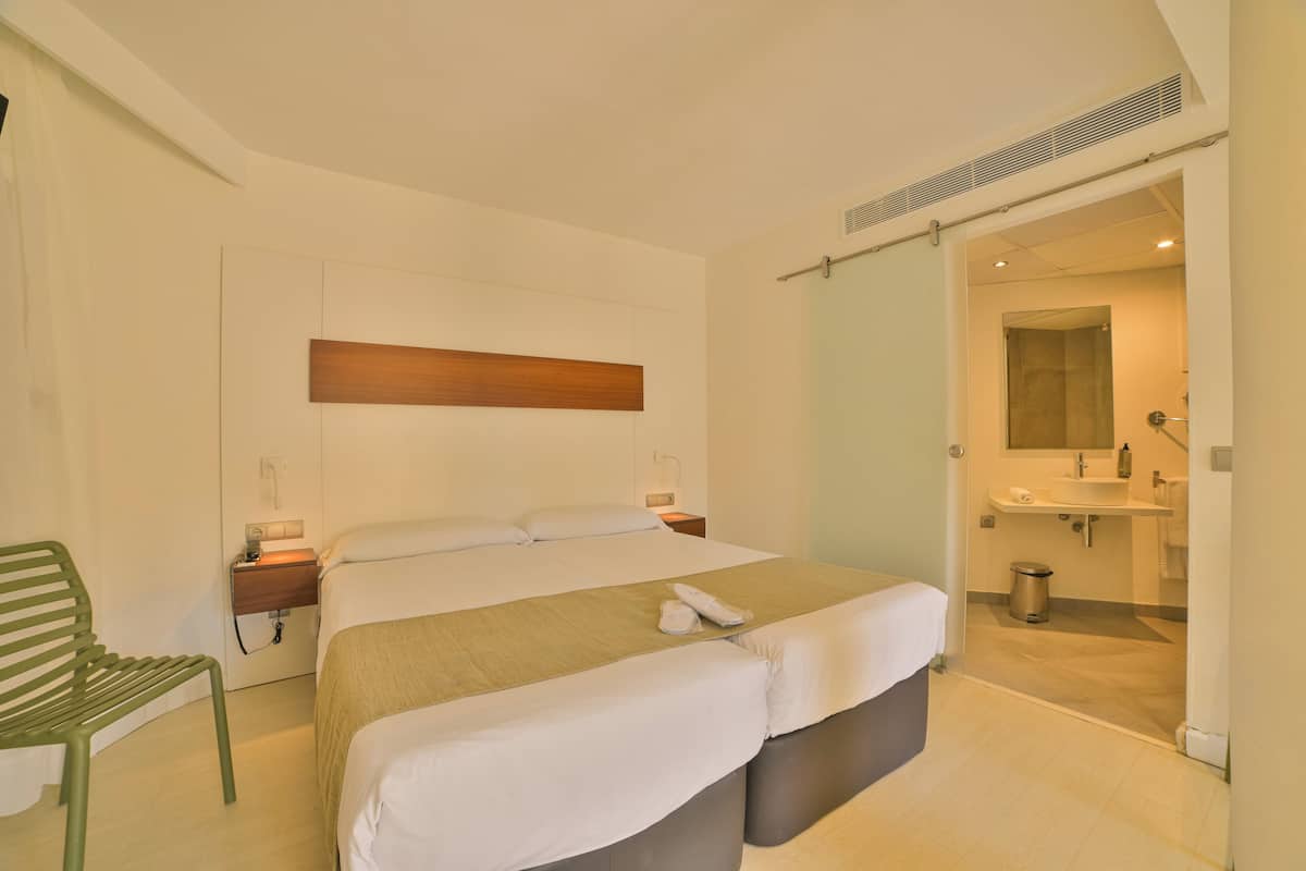 Una camera d'albergo moderna con un letto grande, un comodino, una sedia, un bagno con lavandino e specchio, e un armadio a muro.