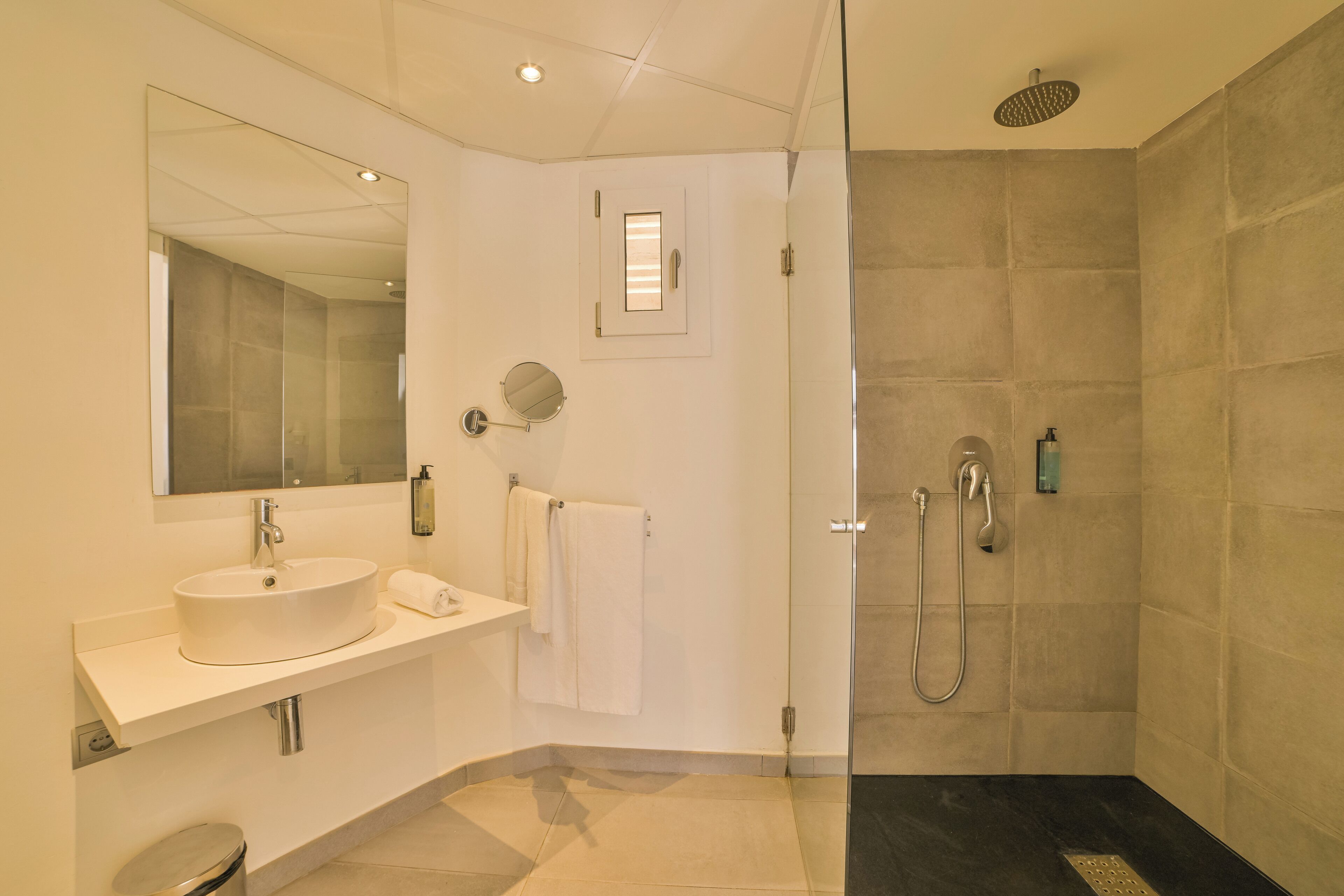 A modern bathroom with a large mirror, a sink, a towel rack, a shower with a handheld showerhead, and a glass-enclosed shower area.