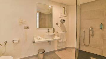 Un baño moderno con ducha envuelta en vidrio, un lavamanos blanco y un espejo grande.