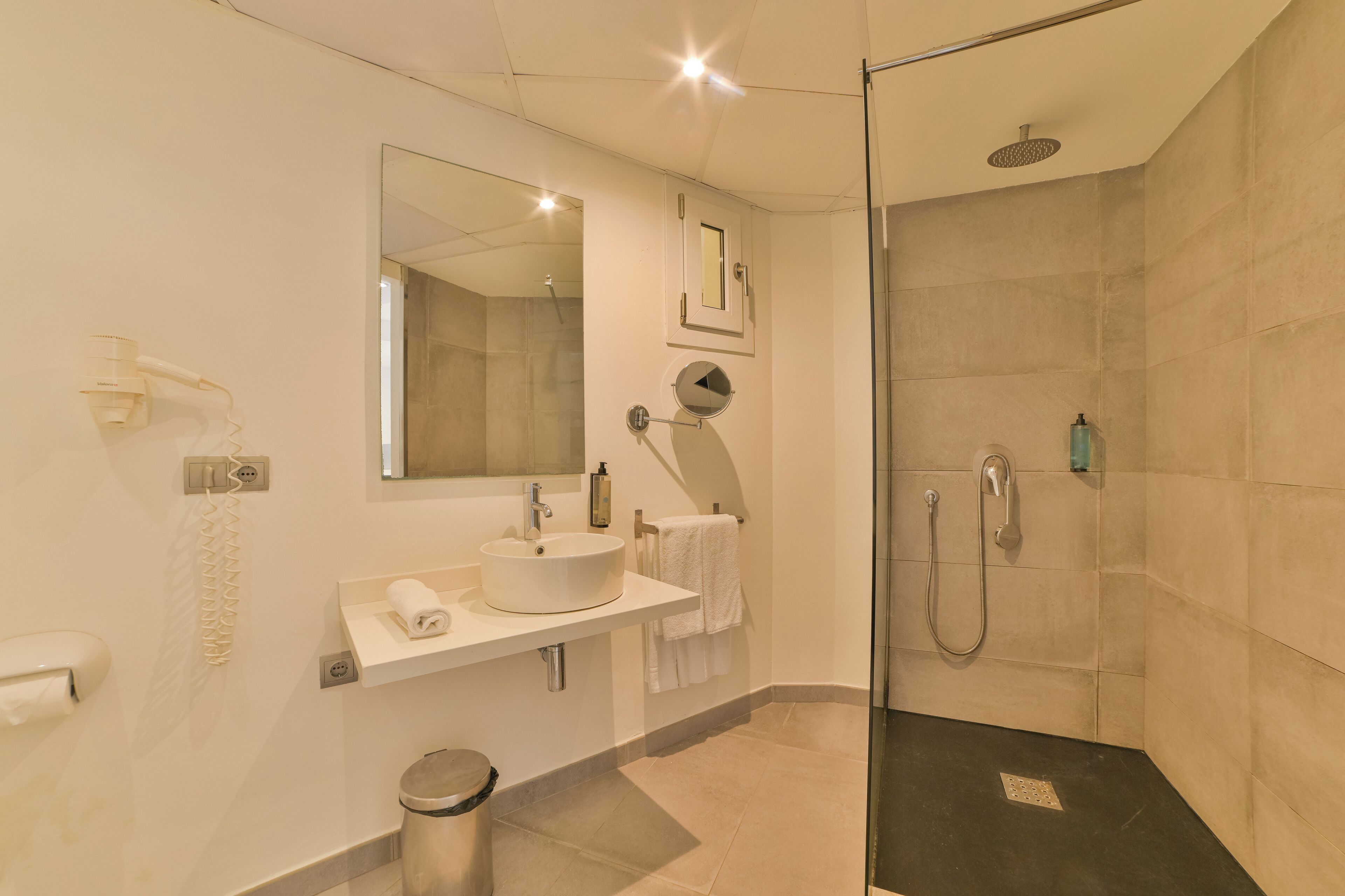 Un baño moderno con ducha envuelta en cristal, lavamanos con espejo y retrete.