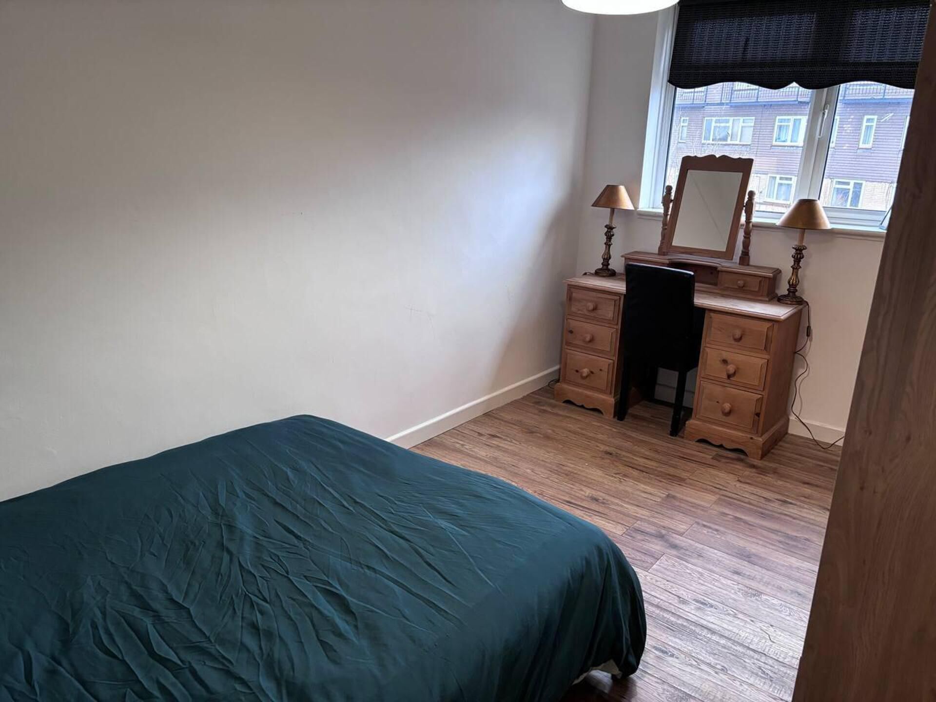 A bedroom with a bed, dresser, chair, and window with blinds.