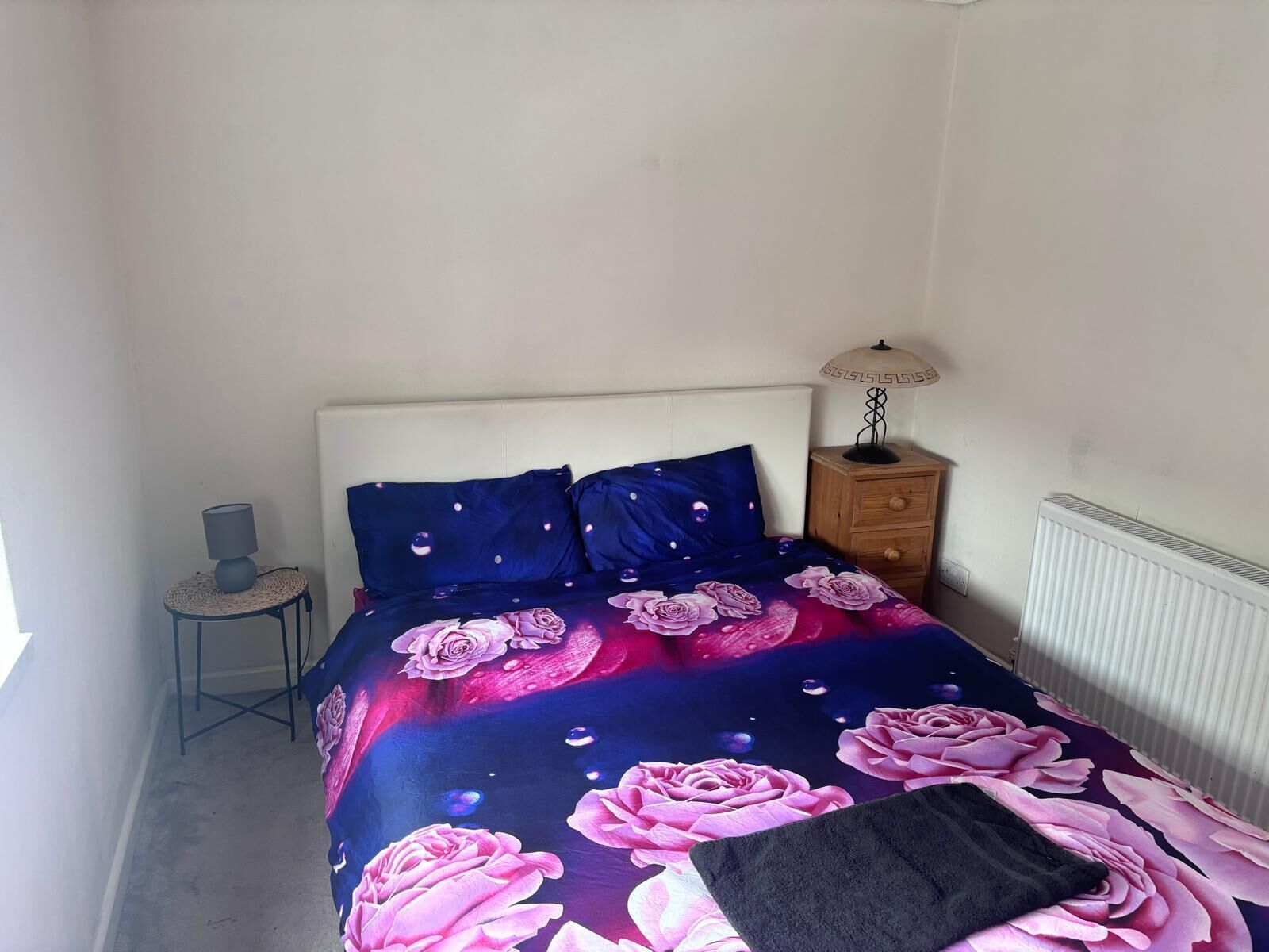 A bedroom with a bed, a bedside table with a lamp, and a radiator.