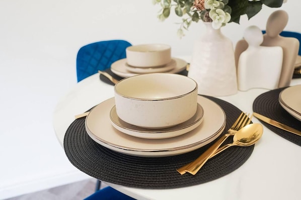 A dining table set with white plates, bowls, and gold cutlery. - Immaculate 4-bed House in Kings Norton (Birmingham)