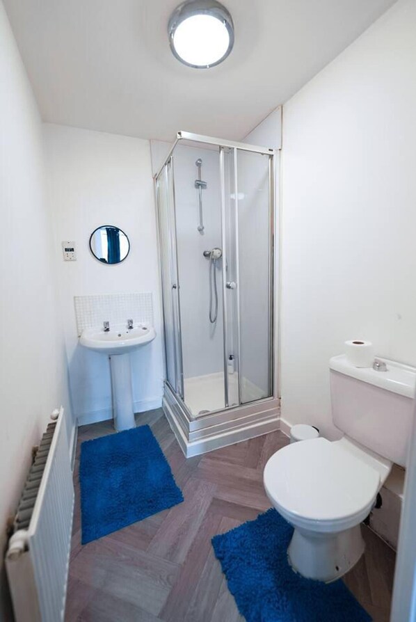 A compact bathroom with a glass-enclosed shower, a pedestal sink, and a toilet. - Immaculate 4-bed House in Kings Norton (Birmingham)