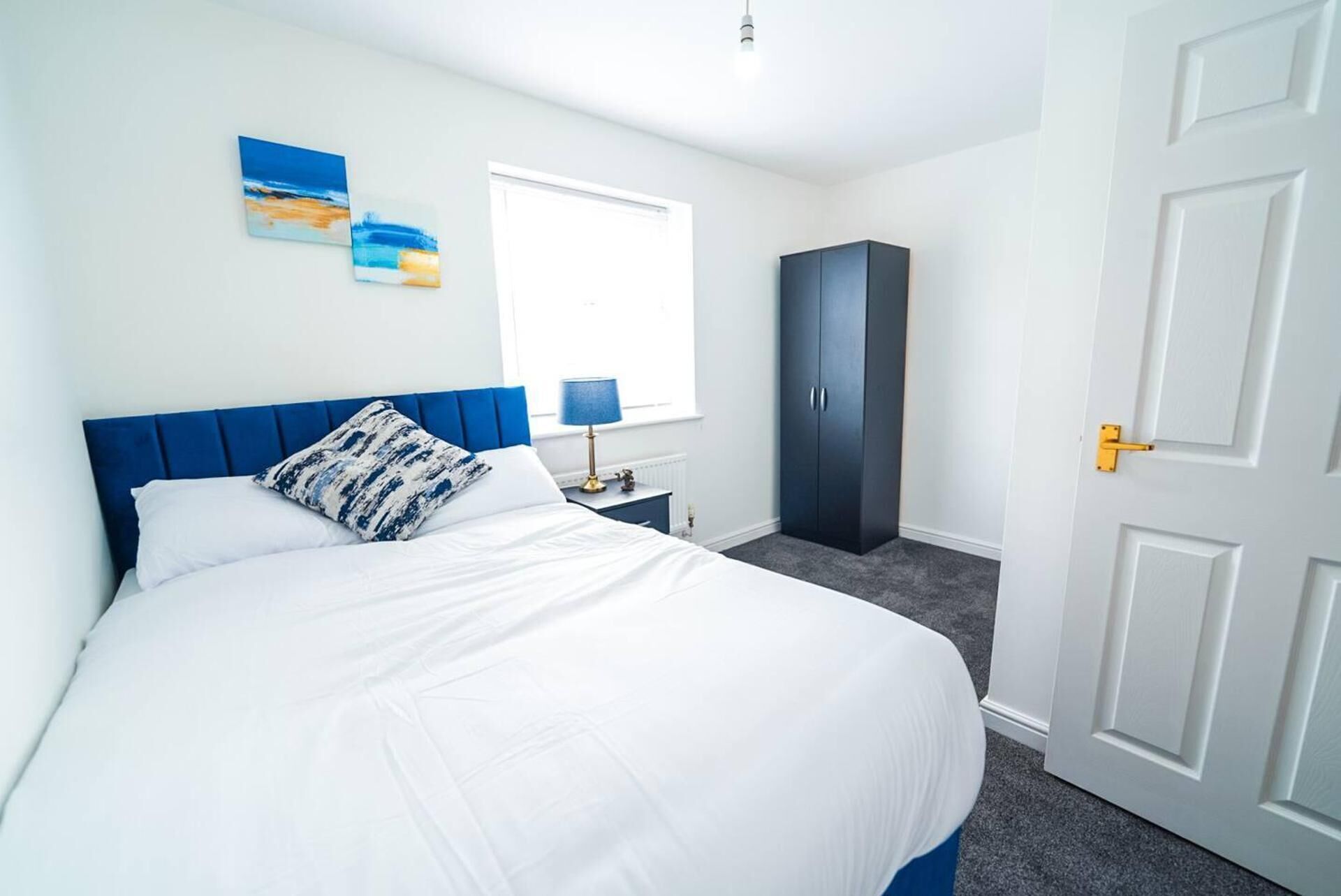 A bedroom with a bed, a wardrobe, a nightstand, and a window.