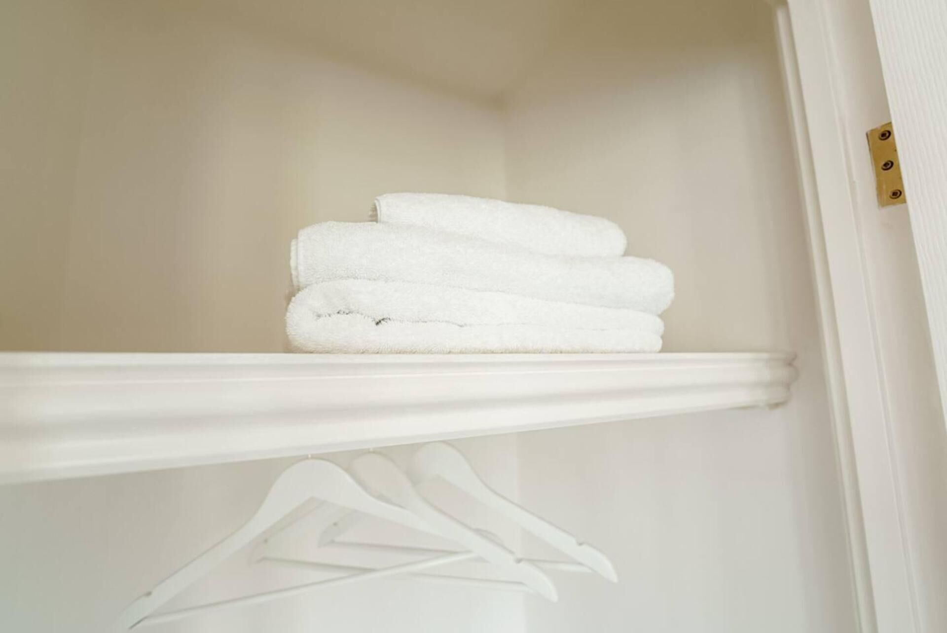 A white closet with a shelf holding folded white towels.
