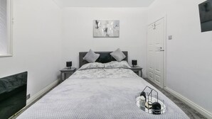 A bedroom with a bed, two bedside tables with lamps, a white door, and a painting on the wall.
