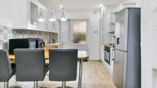 A compact kitchen with white cabinets, a built-in oven, a refrigerator, and a dining area with a wooden table and black chairs.