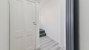 A hallway with a white door, a staircase with grey steps, and a grey wall.