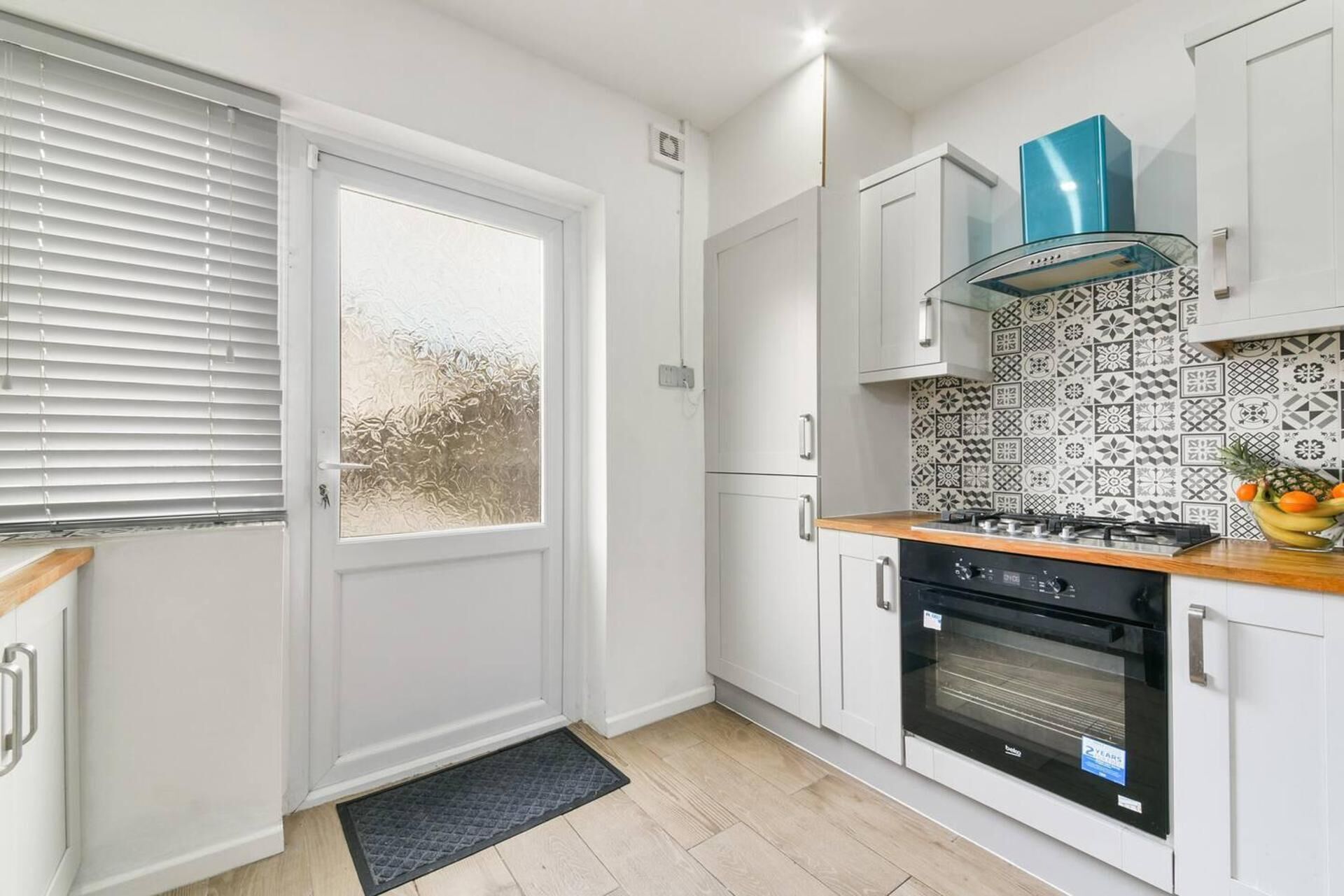 Eine kleine Küche mit weißen Schränken, einem schwarzen Backofen und einer ornamentierten Spritzschutzwand.