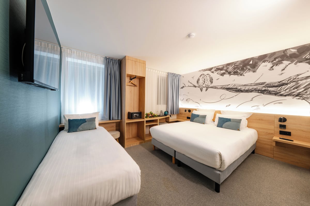 A hotel room with two single beds, a wooden wardrobe, a desk, and a large wall mural.
