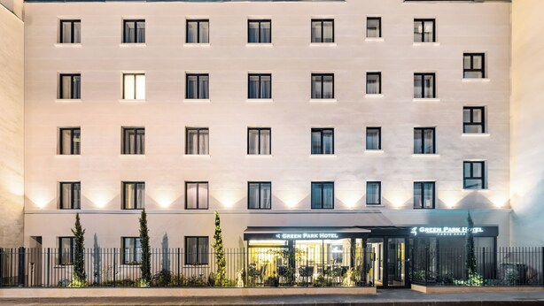 Un hotel de varios pisos con fachada plana, ventanas regularmente distribuidas y una entrada central con un letrero que dice "Green Park Hotel".