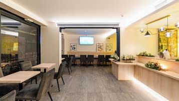 A modern hotel lobby with a reception desk, seating area, and a television screen.