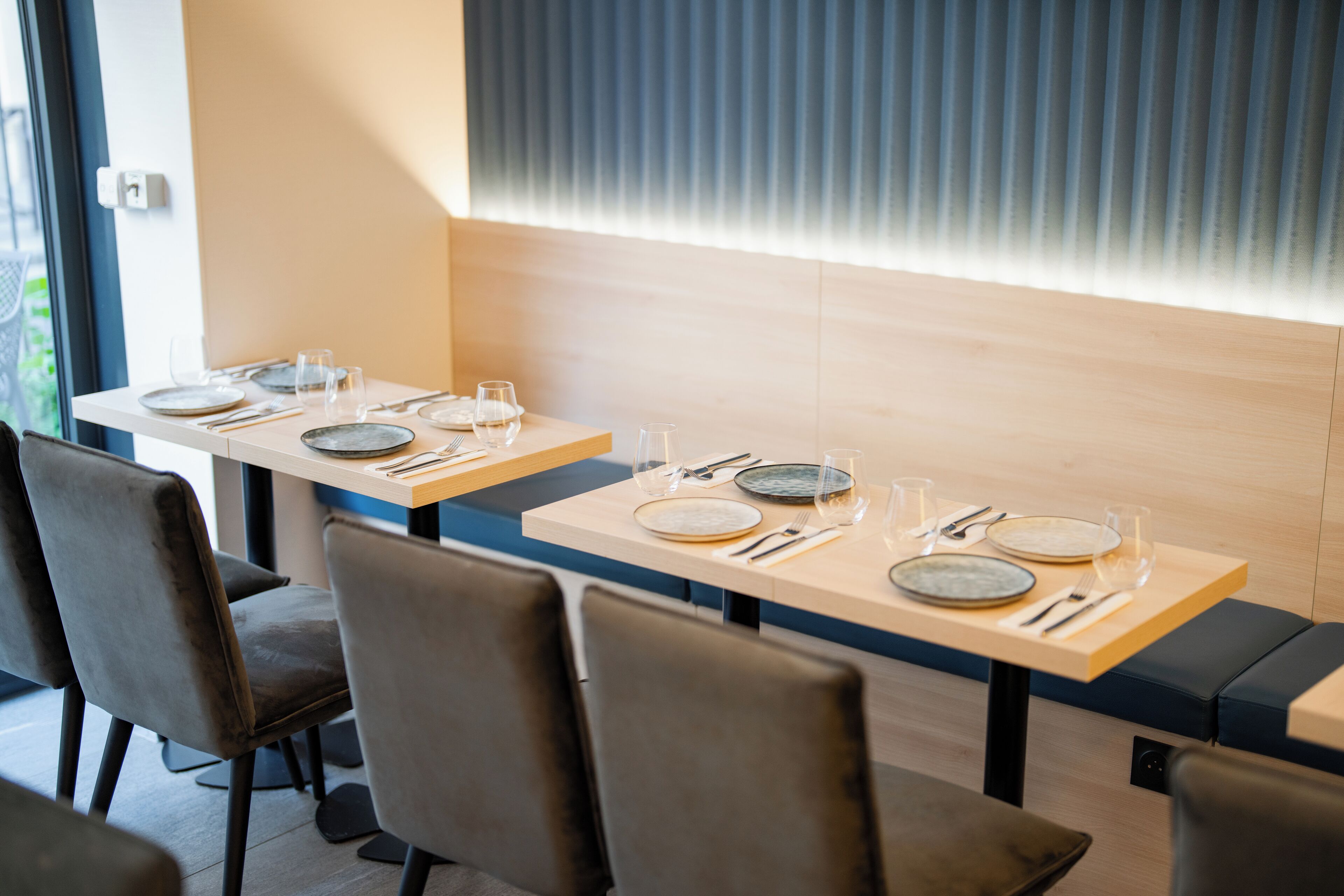 A restaurant with two long tables, each with a set of plates, cutlery, and glasses.