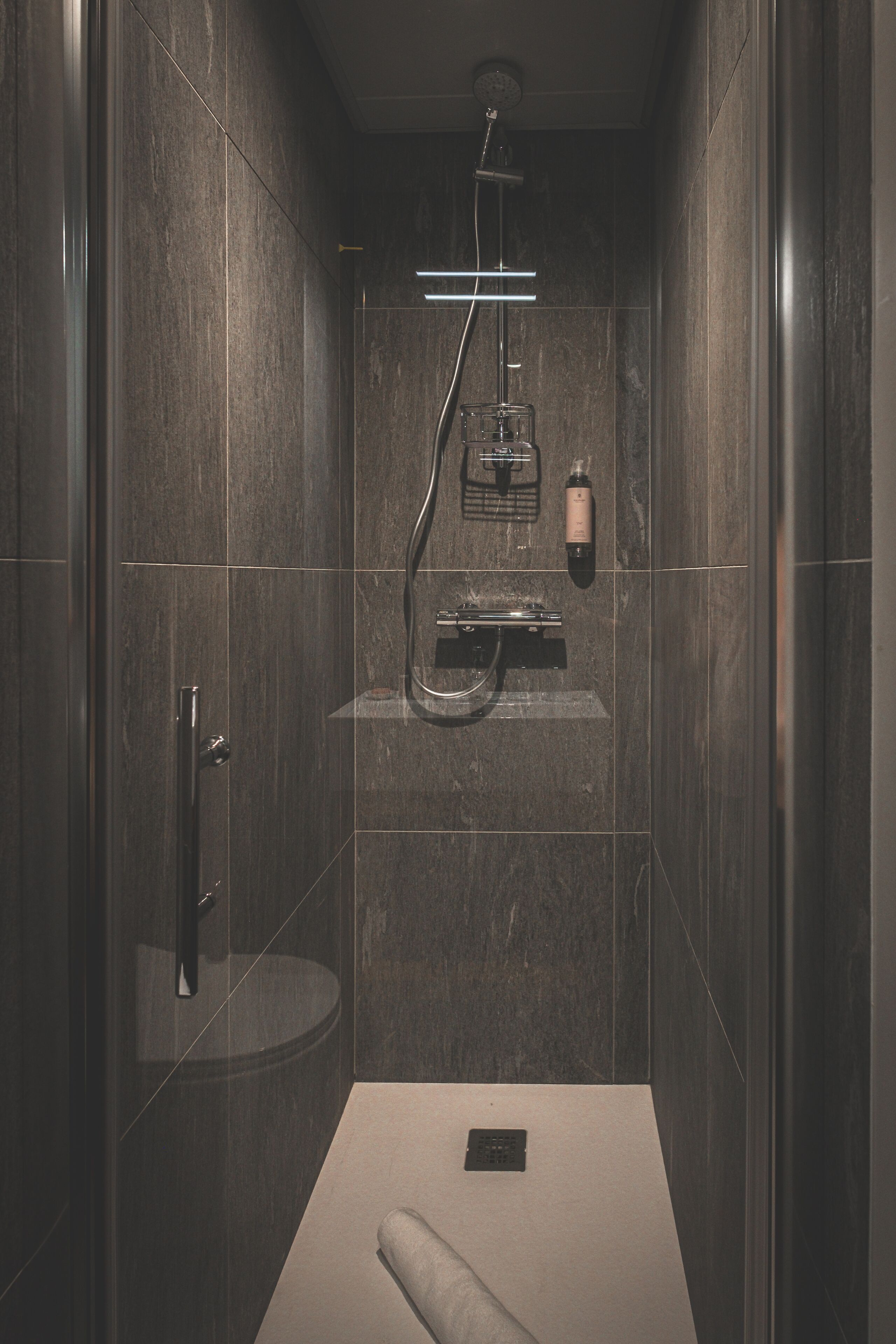 A modern shower with a handheld showerhead, a built-in soap dispenser, and a glass-enclosed shower area.