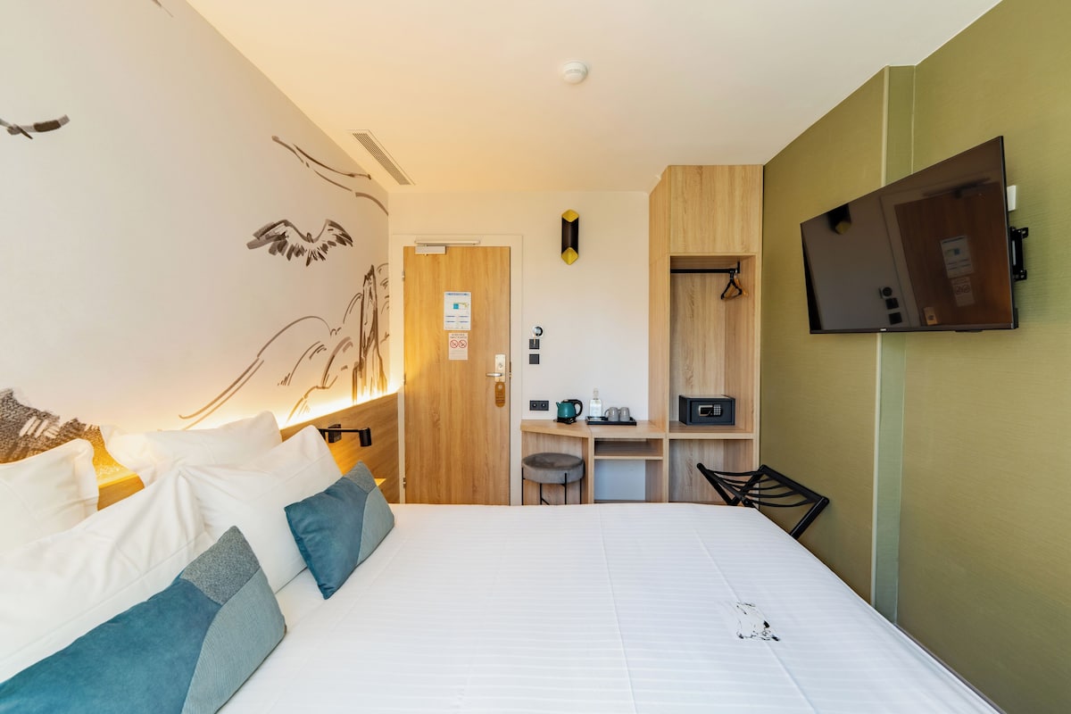 A hotel room with a bed, a desk, a chair, a television, and a mirror.