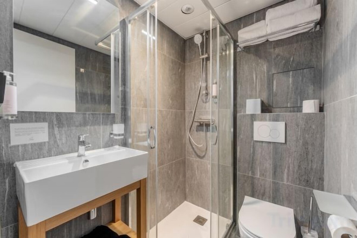 Un baño moderno con cabina de ducha de vidrio, lavamanos blanco y un inodoro.