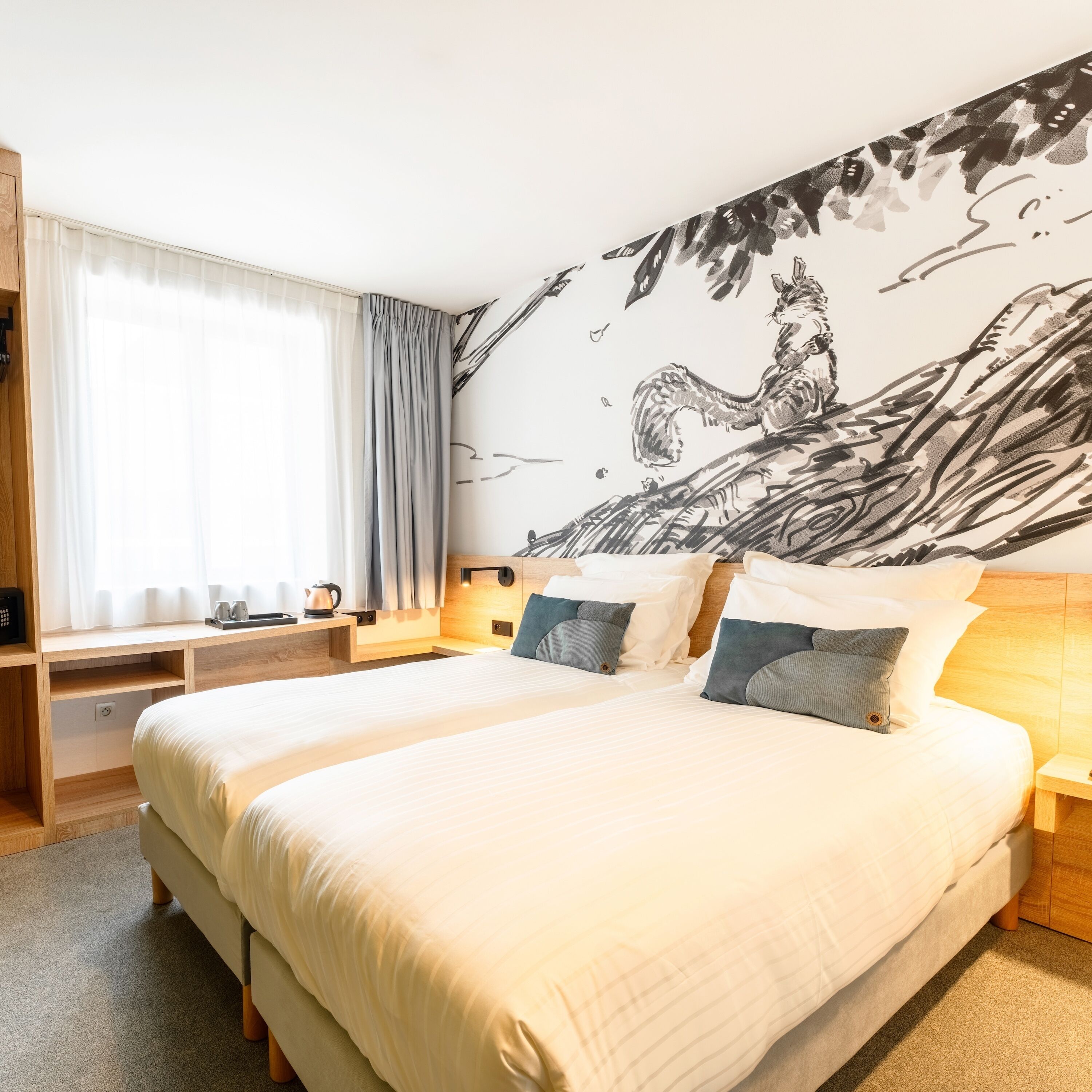 Une chambre d’hôtel moderne avec un grand lit, un bureau doté d’une bouilloire et une fresque murale.