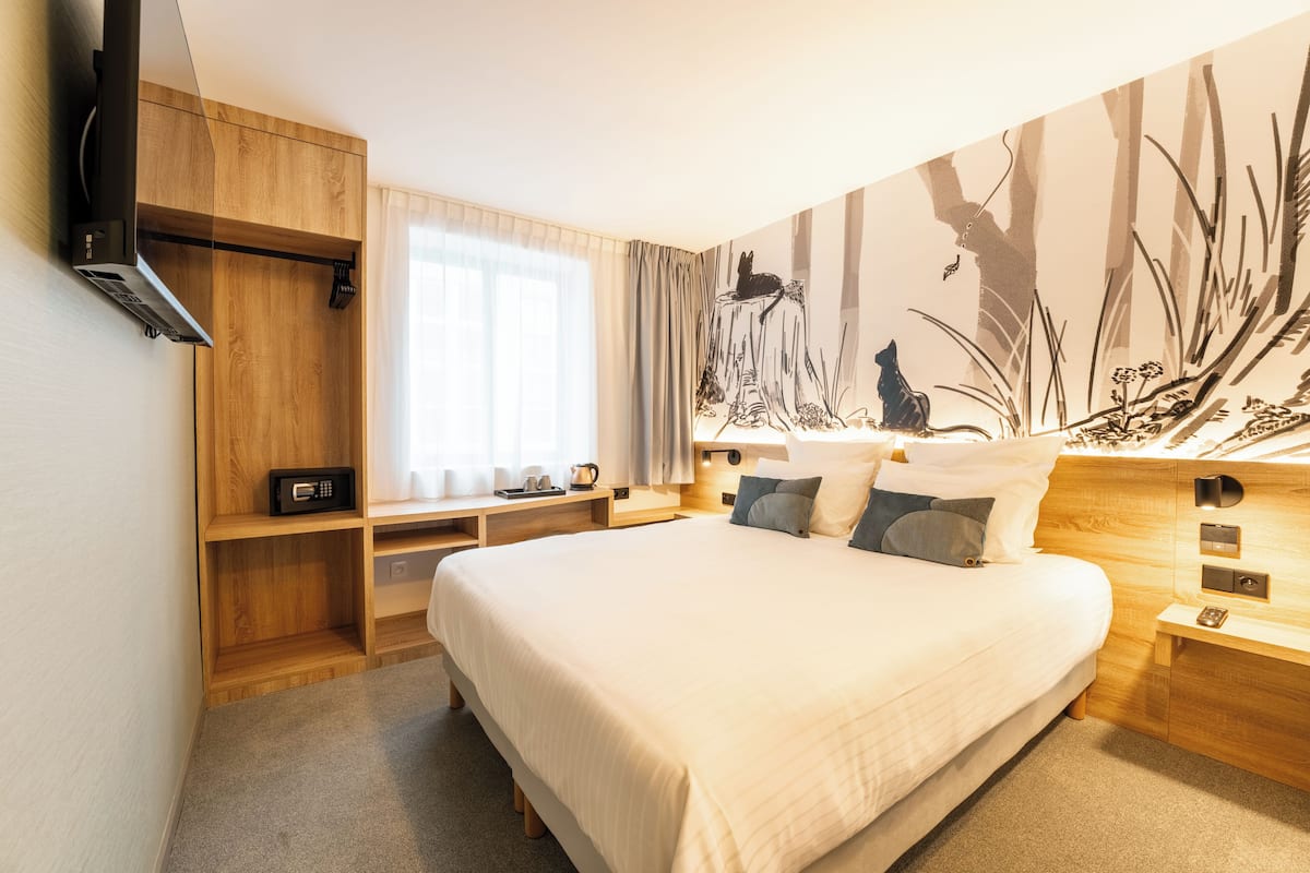 A modern bedroom with a large bed, wooden nightstands, a built-in TV, and a mural on the wall.