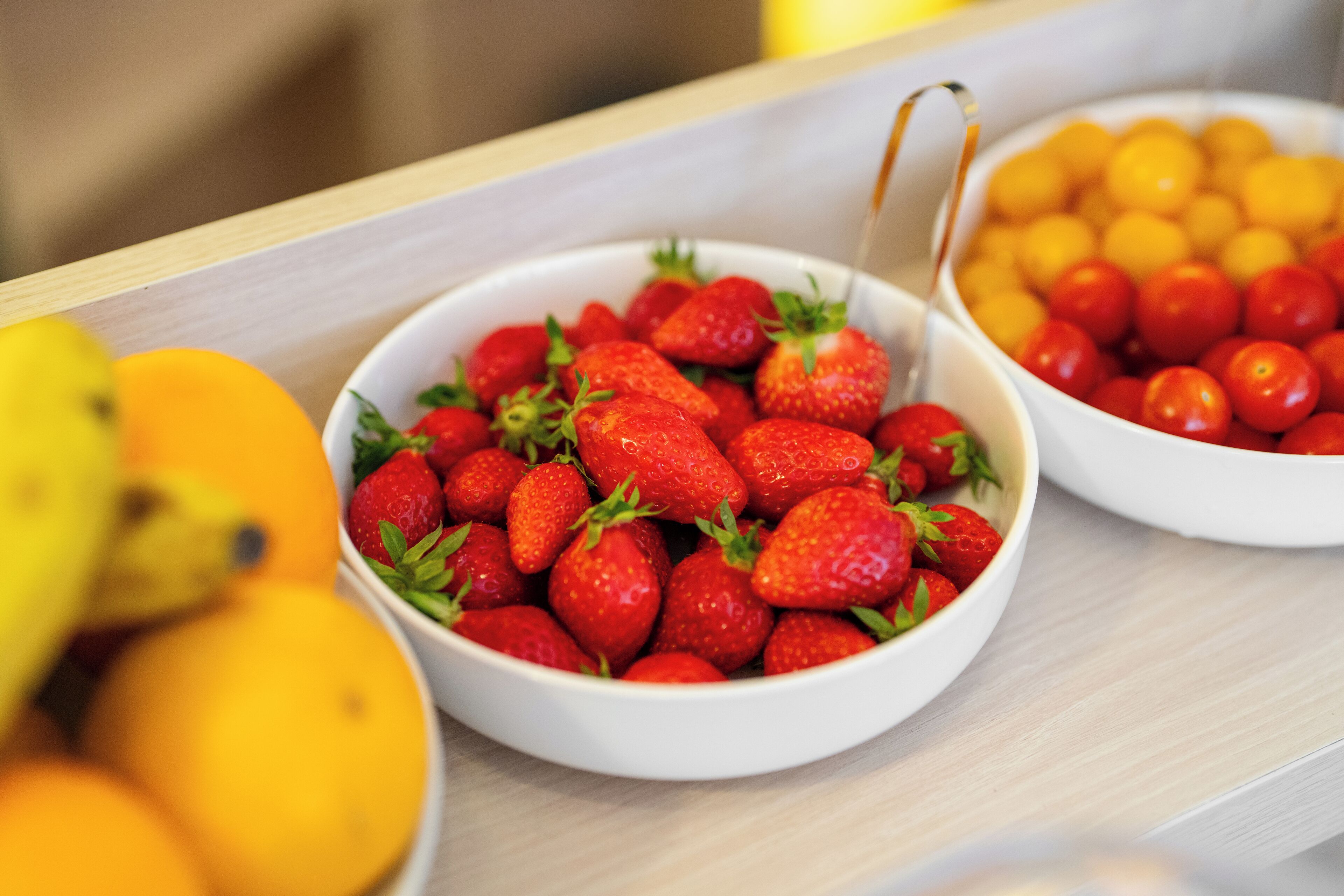 Two bowls of fruit, one with strawberries and the other with cherry tomatoes, on a wooden surface.