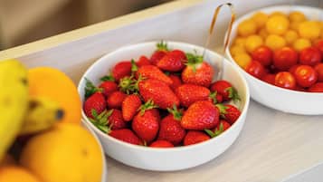 Two bowls of fruit, one with strawberries and the other with cherry tomatoes, on a wooden surface.