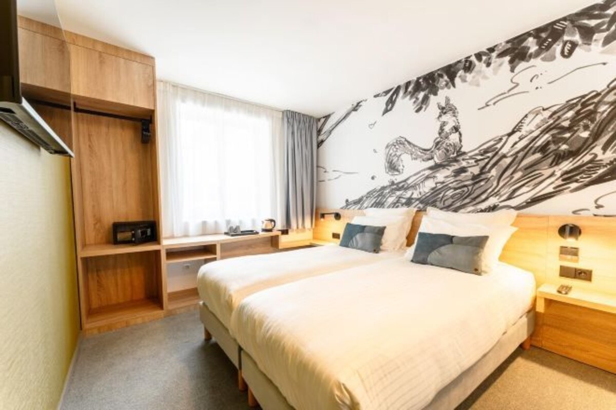 A hotel room with a large bed, wooden furniture, a mural on the wall, and a window with curtains.