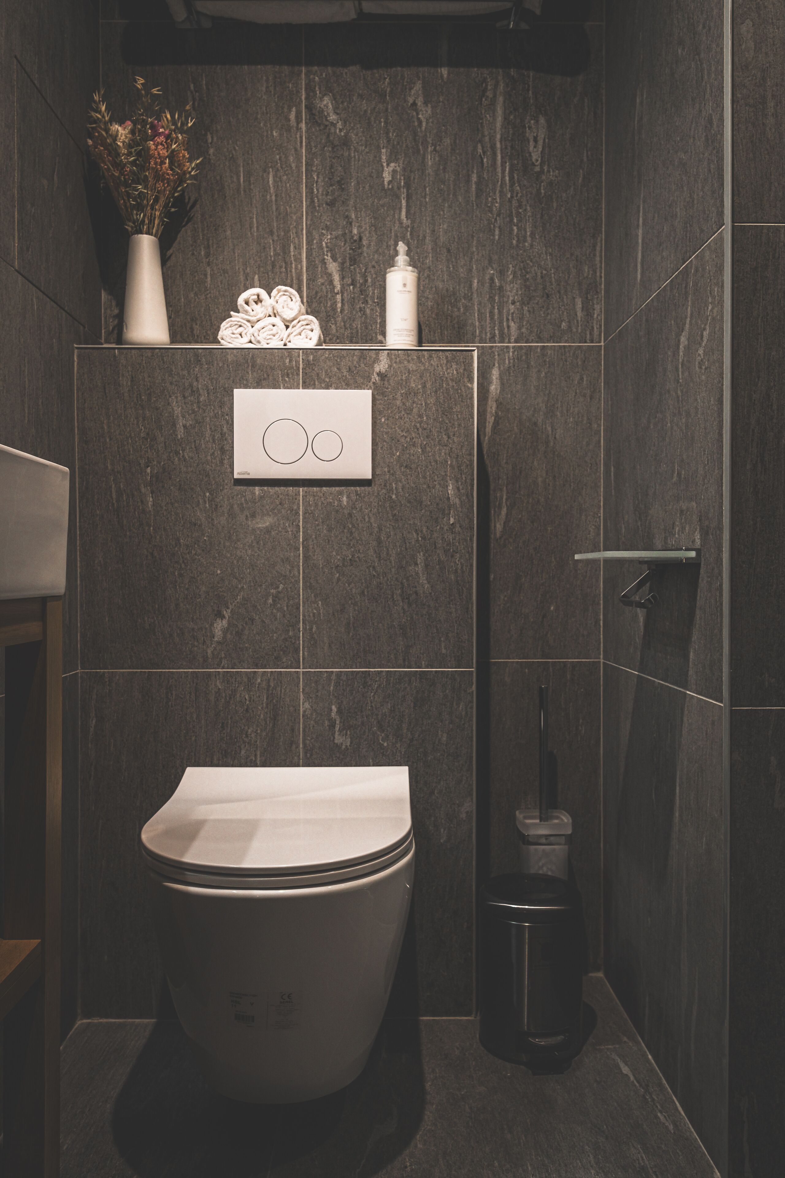 A modern bathroom with a toilet, a trash can, and a towel dispenser.