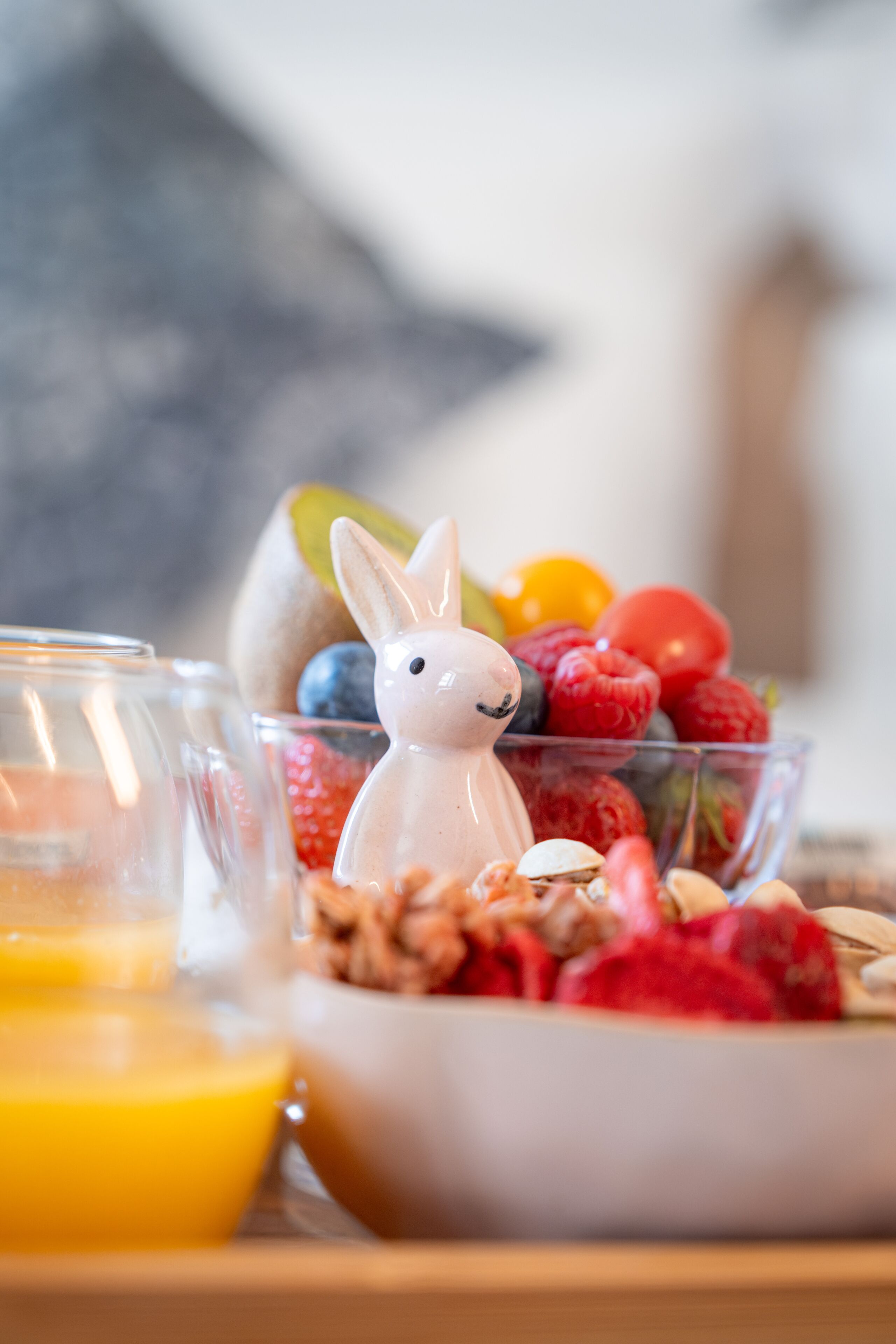 Een ontbijttafel met een glas sinaasappelsap, een schaal gemengd fruit en een keramieken konijnenbeeldje.