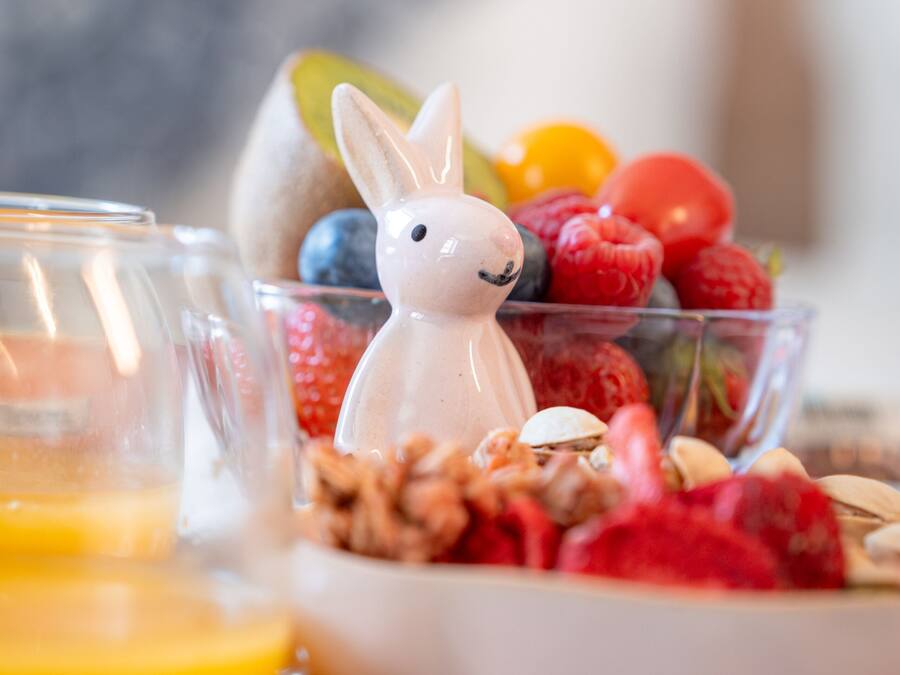 Een ontbijttafel met een glas sinaasappelsap, een schaal gemengd fruit en een keramieken konijnenbeeldje.