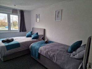 Ein Doppelzimmer mit zwei Betten, einem Fenster mit Vorhängen und zwei gerahmten Bildern von Blättern an der Wand.