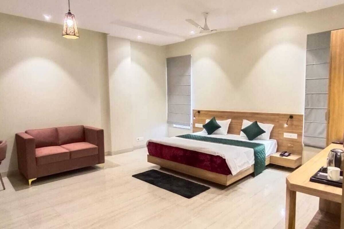 A modern hotel room with a large bed, a sofa, a small table, and a ceiling fan.
