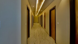 A hallway with a marble floor, wooden doors, and recessed lighting. - Kumaon Inn (Haldwani)