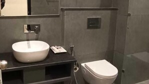 A modern bathroom with a large mirror, a round sink, a toilet, and a glass shower enclosure. - Kumaon Inn (Haldwani)