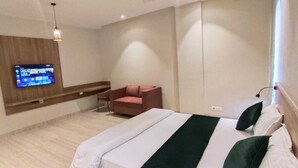 A hotel room with a bed, a TV mounted on the wall, a chair, and a bedside table. - Kumaon Inn (Haldwani)