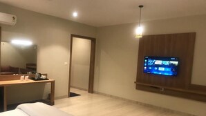 A hotel room with a bed, a desk, a television mounted on the wall, and a wooden panel. - Kumaon Inn (Haldwani)