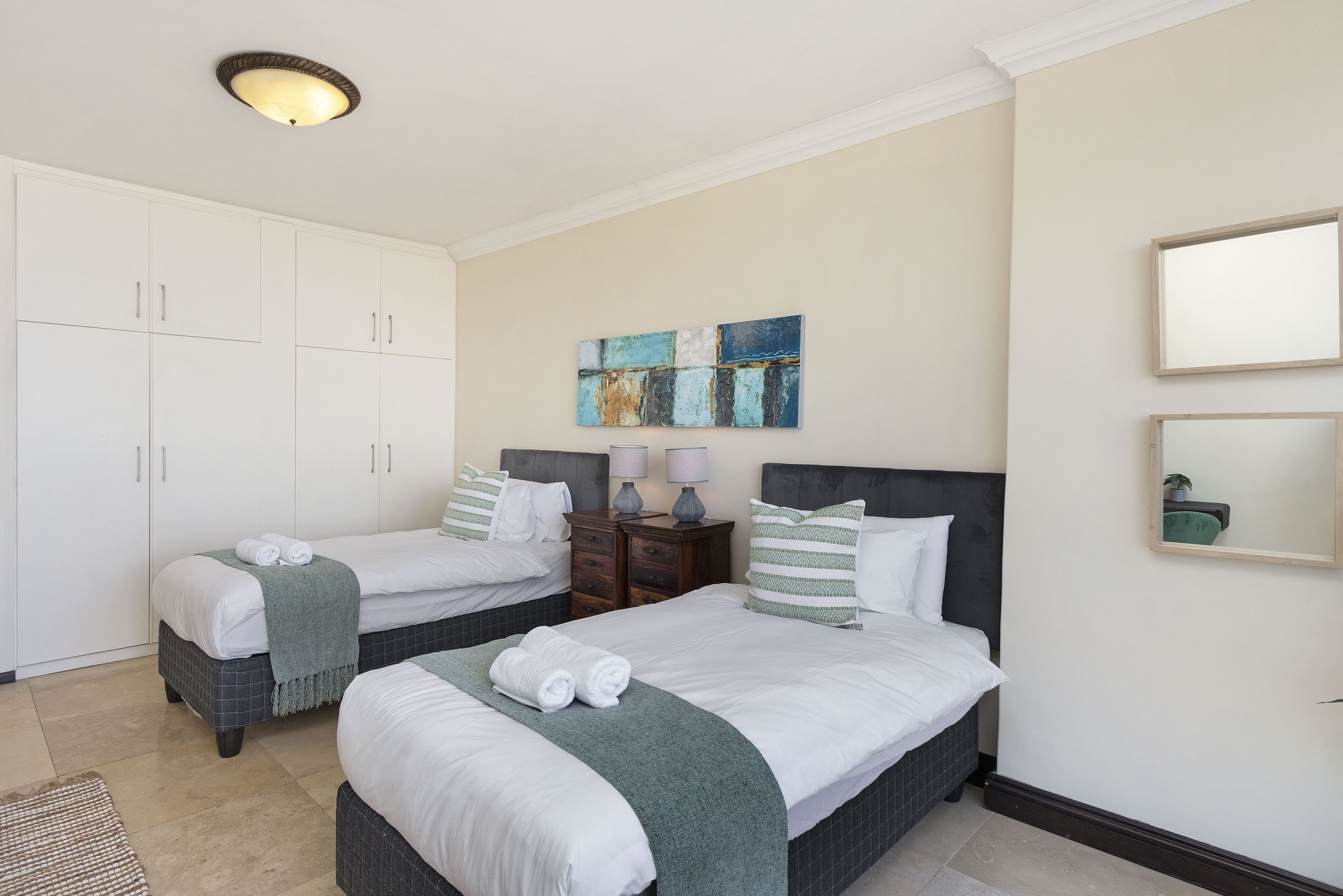 A hotel room with two beds, a wardrobe, a painting, and a mirror.