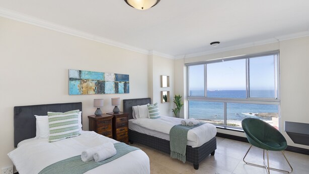 A hotel room with two beds, a view of the ocean, and a green chair. - Blouberg Heights 603 (Cape Town)