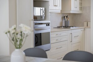 A modern kitchen with stainless steel appliances, white cabinetry, and a vase with white flowers on the table. - Blouberg Heights 603 (Cape Town)