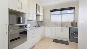 A modern kitchen with white cabinets, stainless steel appliances, and a large window. - Blouberg Heights 603 (Cape Town)