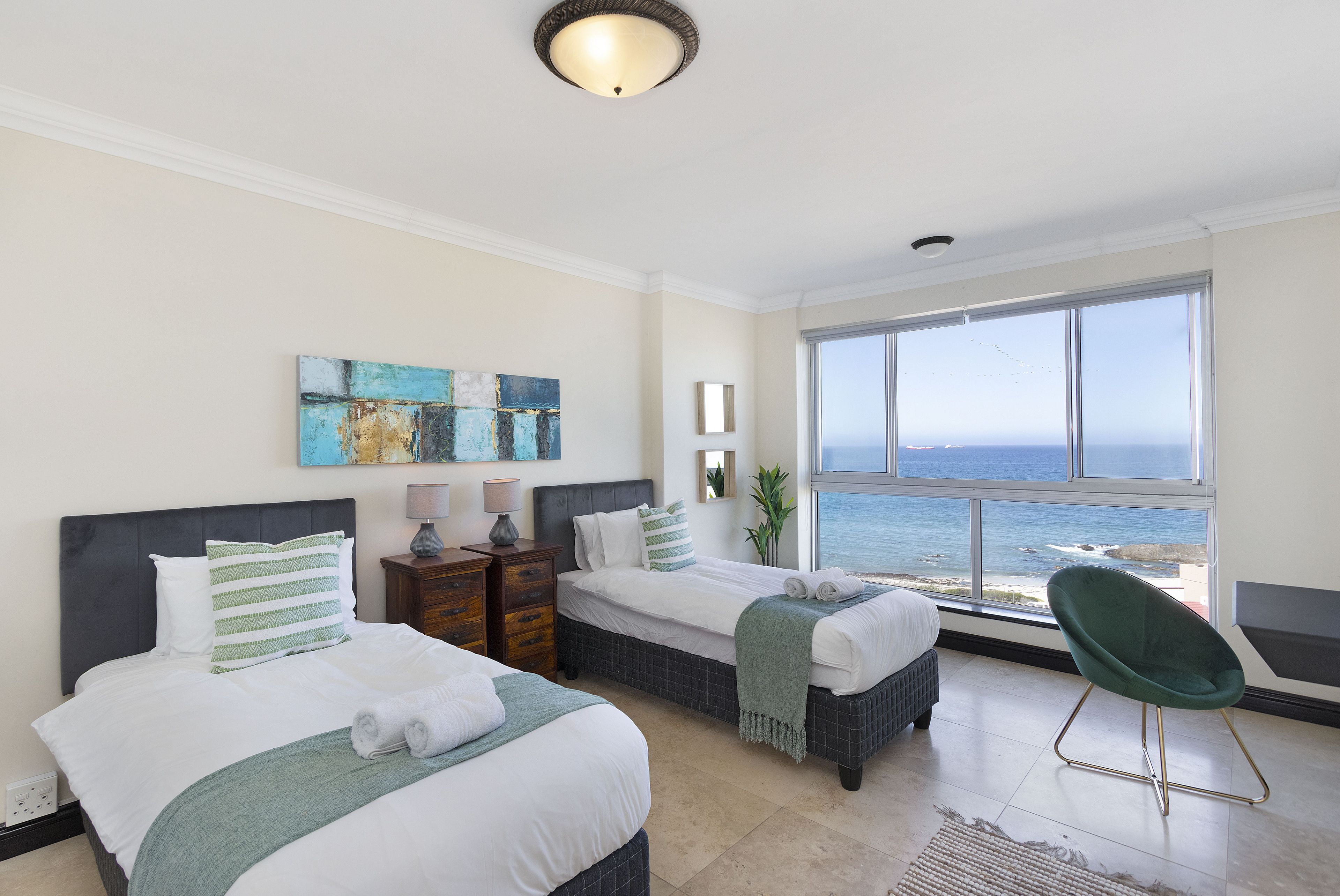 A hotel room with two beds, a view of the ocean, and a green chair.