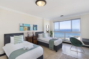 A hotel room with two beds, a view of the ocean, and a green chair. - Blouberg Heights 603 (Cape Town)
