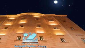 A building with illuminated windows and a sign that reads "By Gulshan Apartments." - Ninety Two (Unaizah)