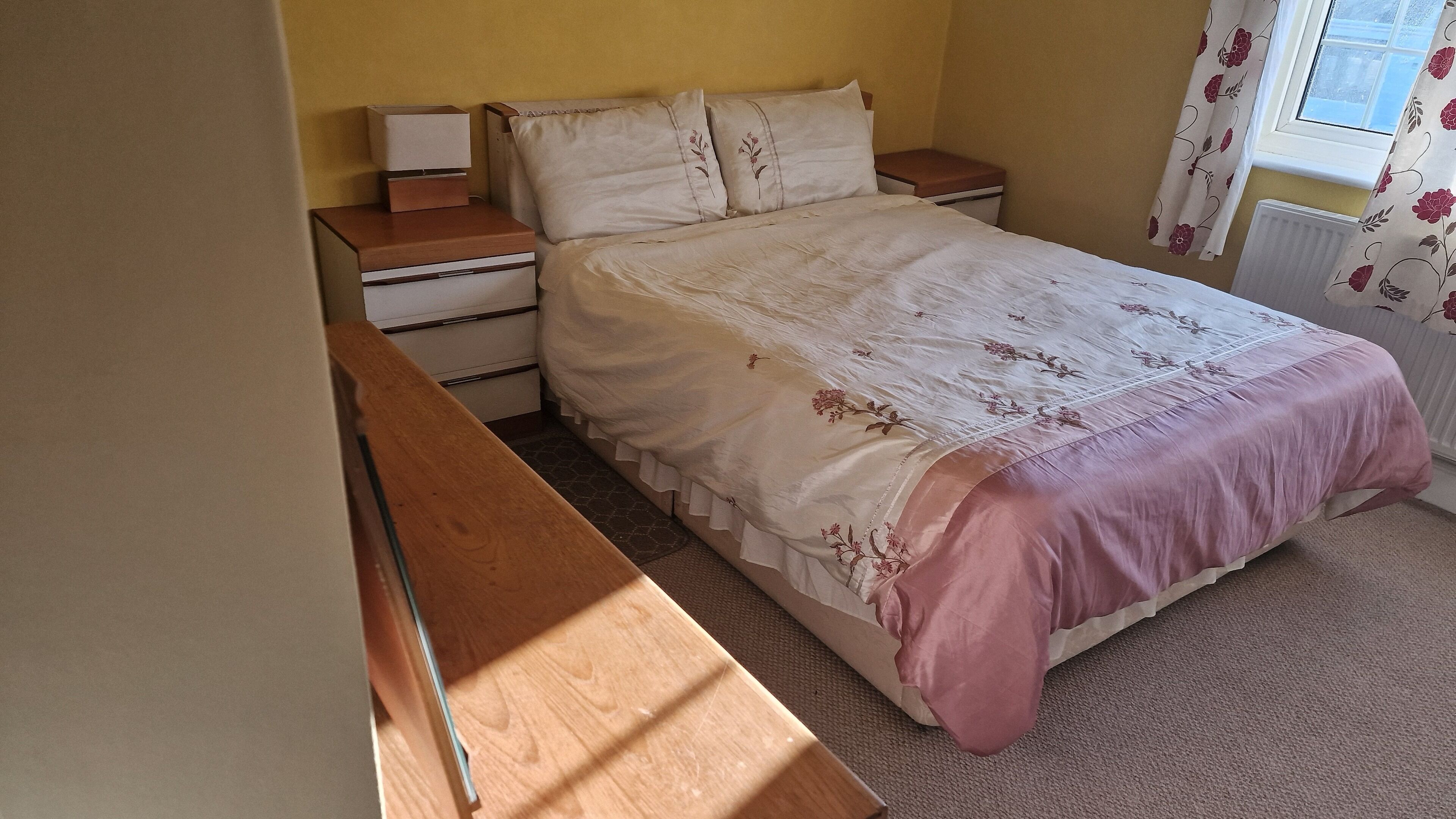 A bedroom with a bed, nightstands, a dresser, and a window with curtains.