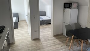 Una habitación moderna y funcional con kitchenette, cama con ropa de cama gris y zona de comedor con mesa y sillas.
