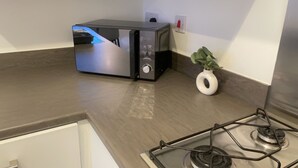 Un four à micro-ondes compact est posé sur un plan de travail de cuisine, avec une cuisinière en acier inoxydable en dessous.
