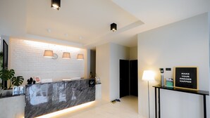 A modern reception desk with a marble top, a clock, and a motivational poster. There are two pendant lights above the desk, and a floor lamp to the right. - Get Guesthouse 3  (Hat Yai)