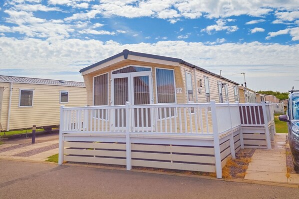 A mobile home with a fenced deck, a large window, and a number '82' on the side.