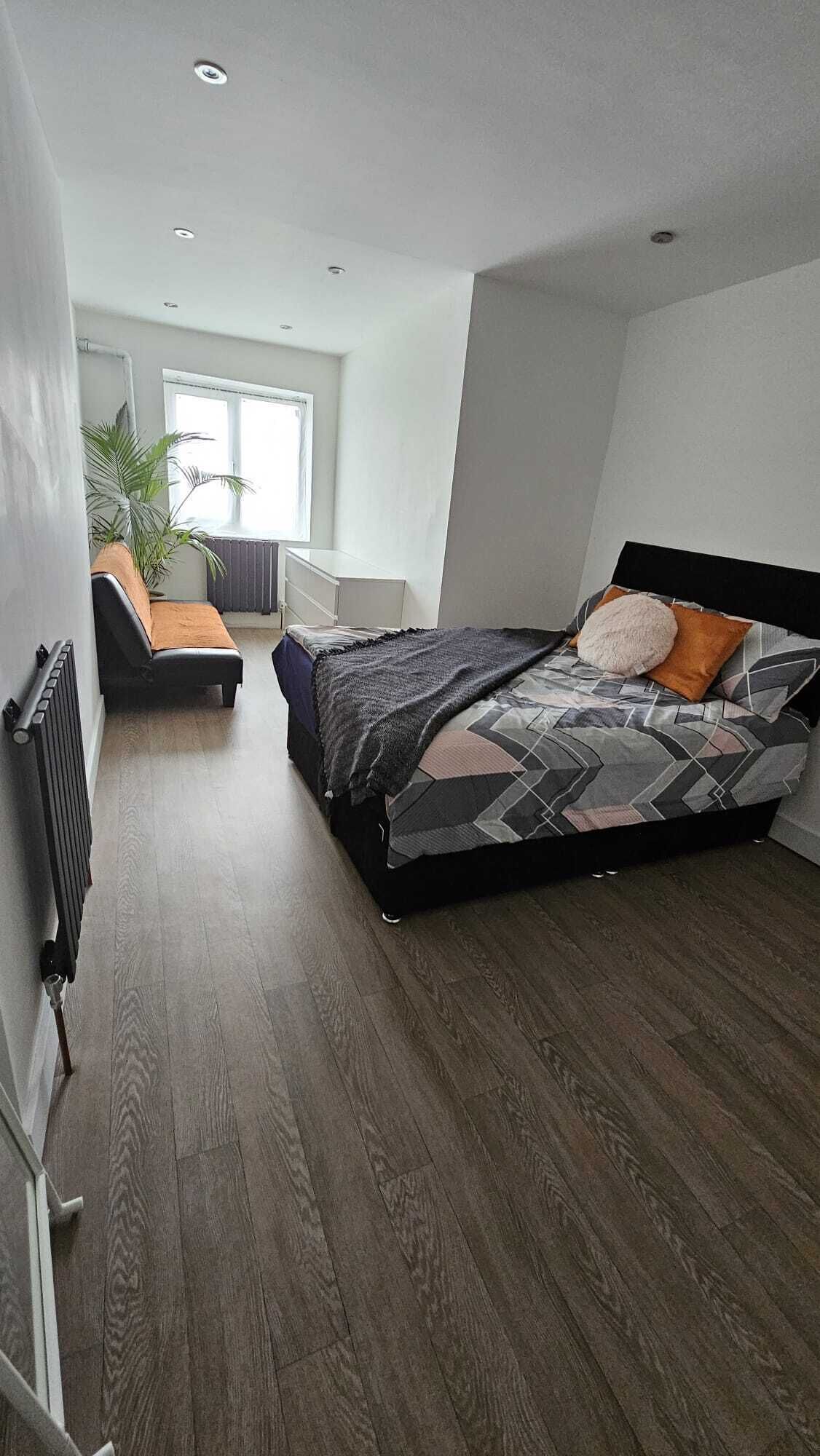 A modern bedroom with a large bed, a small sofa, and a radiator.